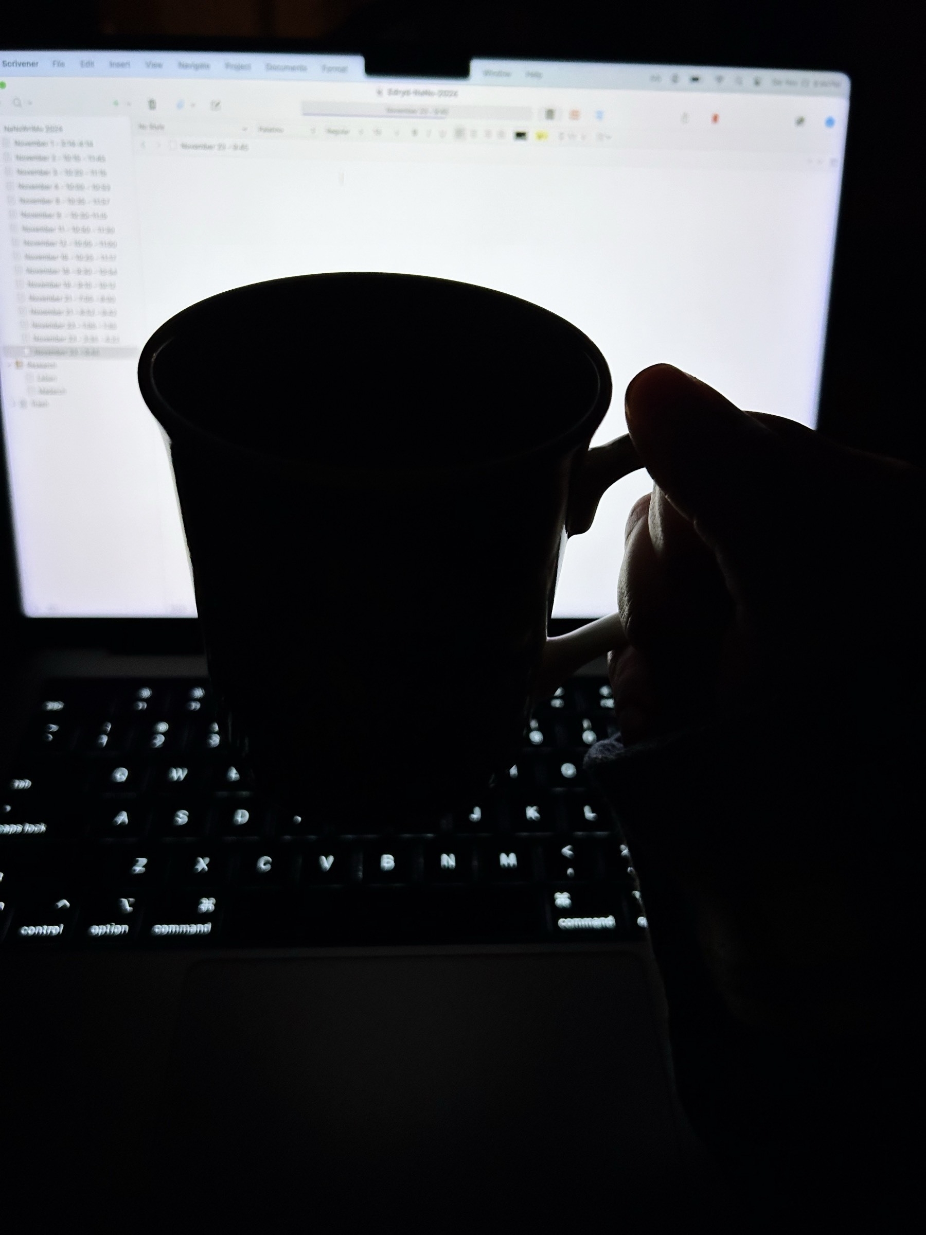 Silhouette of a small mug held in front of an illuminated laptop screen. A word processor is open. 